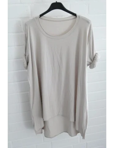 Beigefarbenes Damen Shirt mit Rundhals. Vorne kurz hinten lang vor weißer Wand.