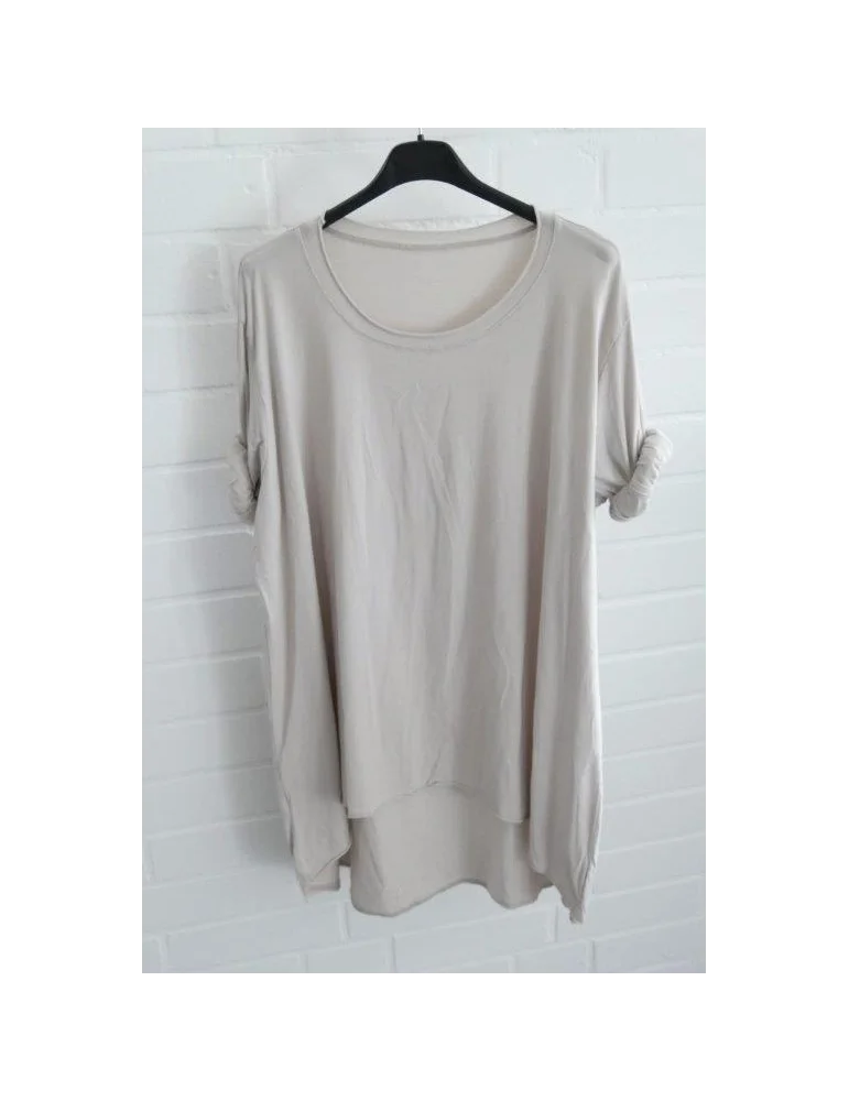 Beigefarbenes Damen Shirt mit Rundhals. Vorne kurz hinten lang vor weißer Wand.