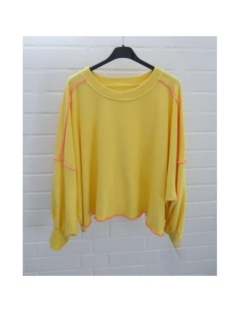 Gelbes Oversized Sweatshirt mit neon-pinken Kontrastnähten auf Bügel vor weißer Wand