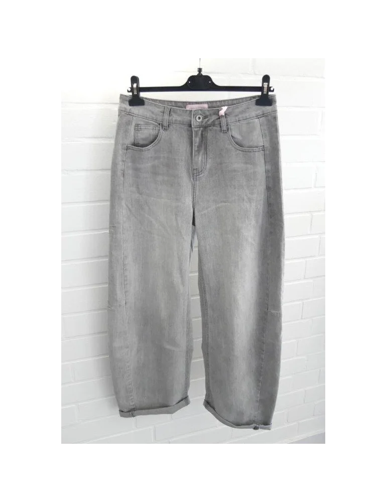 Graue Balloon Jeans mit seitlichen Einsätzen und Umschlägen vor weißer Wand