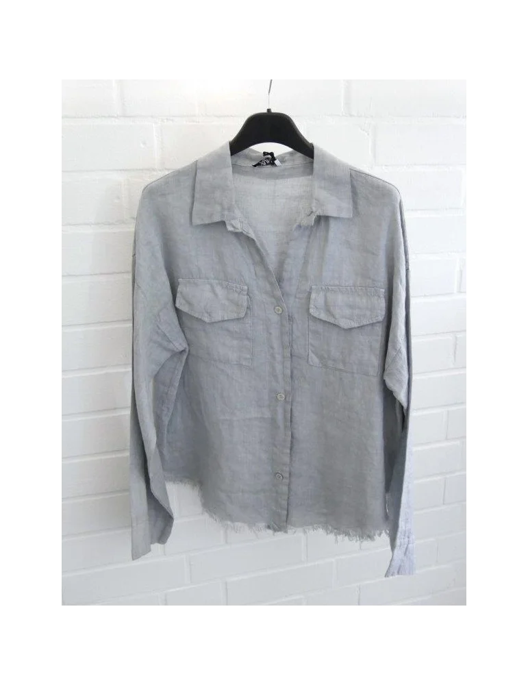 Hellgraue Damen Leinenbluse mit Brusttaschen und ausgefranstem Saum vor weißer Wand.