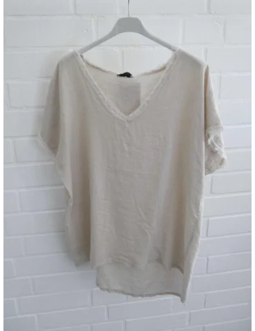Beiges Damen Shirt mit V-Ausschnitt und ausgefransten Kanten vor weißer Wand
