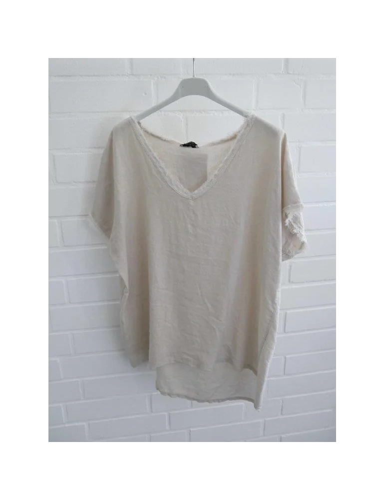 Beiges Damen Shirt mit V-Ausschnitt und ausgefransten Kanten vor weißer Wand