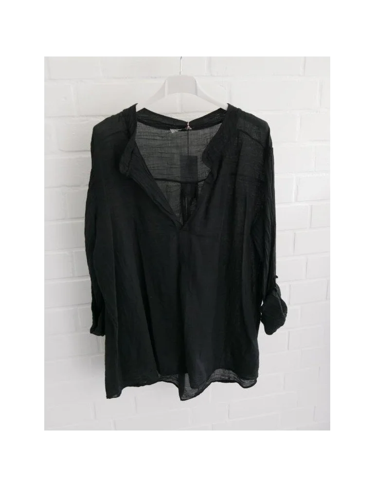 Schwarze Damenbluse mit langen Ärmeln vor weißer Wand