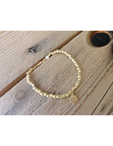 Goldfarbenes Armband mit kleine unegealen Würfeln auf Holzuntergrund