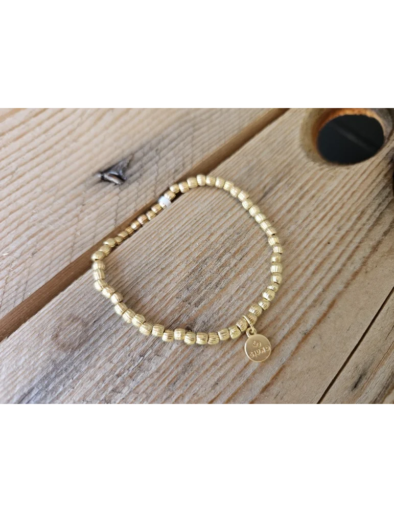 Goldfarbenes Armband mit kleine unegealen Würfeln auf Holzuntergrund