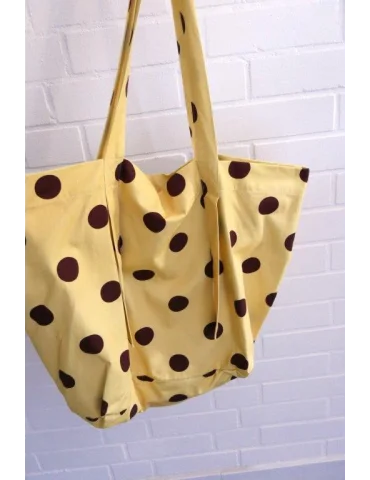 Gelbe Stofftasche mit braunen Punkten und langen Tragehenkeln vor einer weißen Wand
