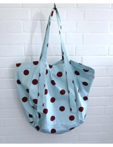 Hellblaue Stofftasche mit braunen Punkten und langen Tragehenkeln vor einer weißen Wand