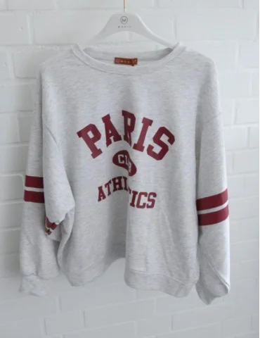 Hellgrau meliertes Paris Athletics Sweatshirt mit weinroten Streifen an den Ärmeln an einem Bügel