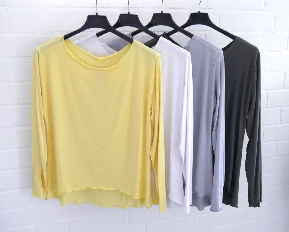 Vier verschiedenfarbige langarm Shirts vor einer weißen Wand