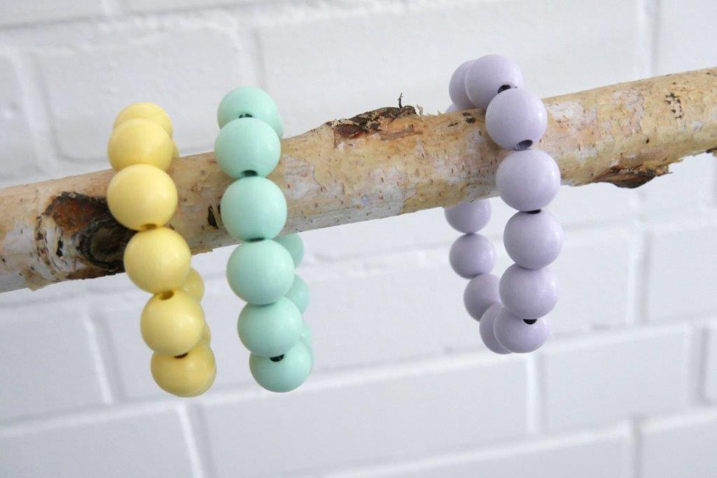 Drei Holzperlen-Armbänder in verschiedenen Farben auf einem Birkenast
