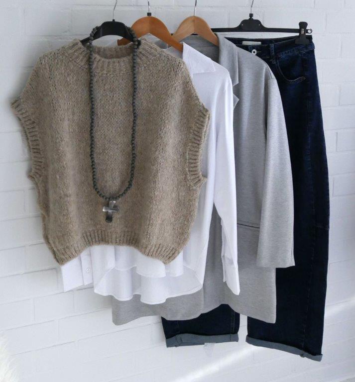 Blaue Barell Jeans mit hellgrauen Oversize Blazer, beigem Pullunder, weißer Bluse und grauer Kreuzkette hängend vor weißer Wand